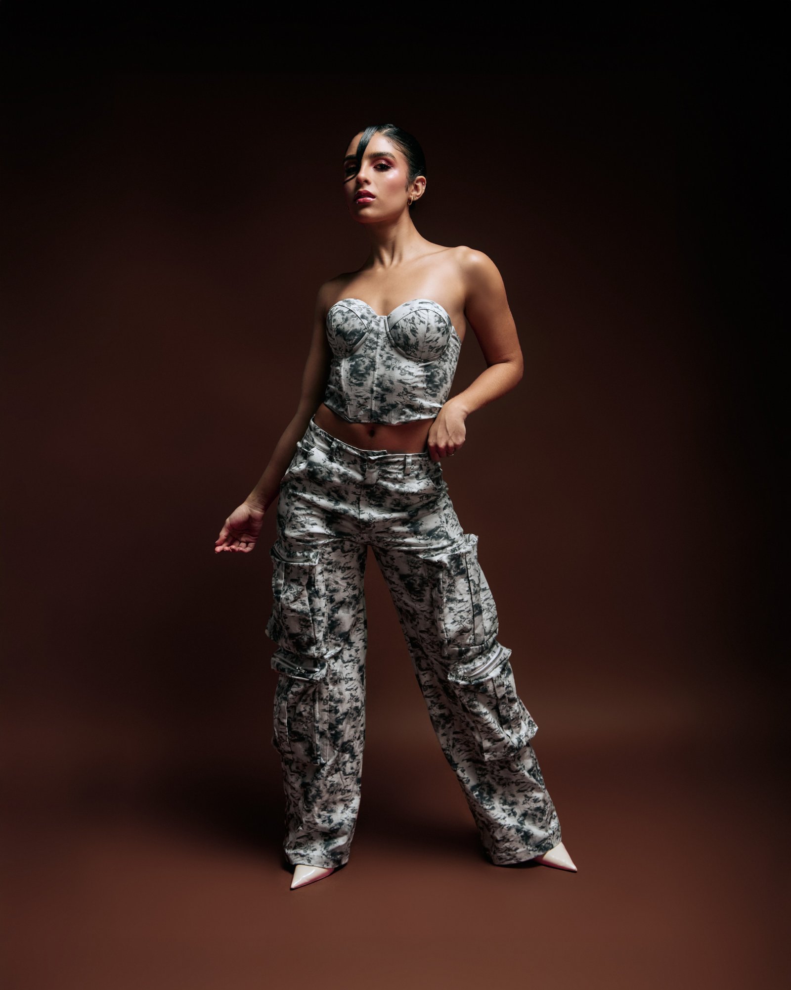 Elegant woman modeling a chic black-and-white patterned crop top and cargo pants on a dark background. Perfect for fashion, streetwear, and runway style photography.