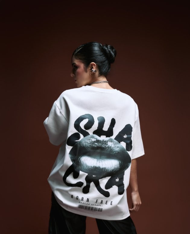 Stylish woman modeling a graphic oversized T-shirt with lips print and bold text, highlighting modern streetwear fashion from Shacra Apparel against a dark gradient background.