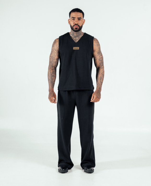 Black sportswear tank top and pants with tattoos, stylish male model showcasing athletic fashion, minimalist background, modern activewear lifestyle, SHACRA branding prominently displayed.