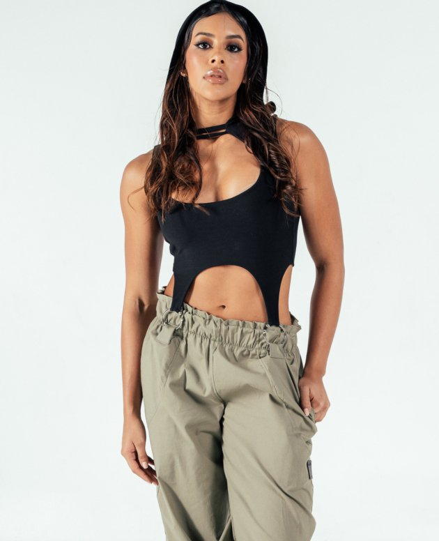 Striking woman with long wavy hair wearing stylish black cutout top and beige cargo pants, showcasing trendy fashion and confident attitude. Perfect for fashion-forward looks and street style inspiration.